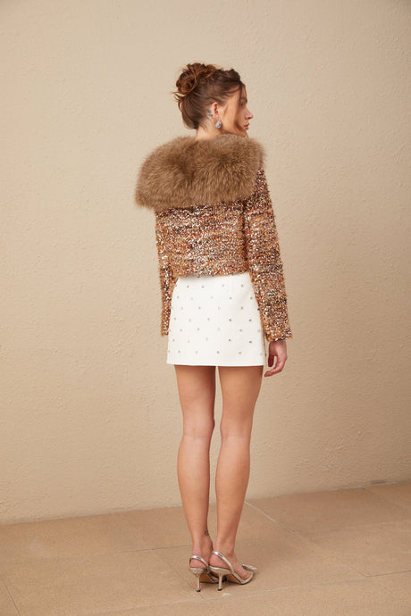 Woman wearing gold sequined jacket with fur trim glittering in light
