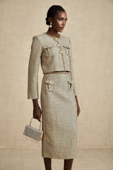Woman wearing gold tweed sequin jacket and matching skirt set by Aelle standing against plain background