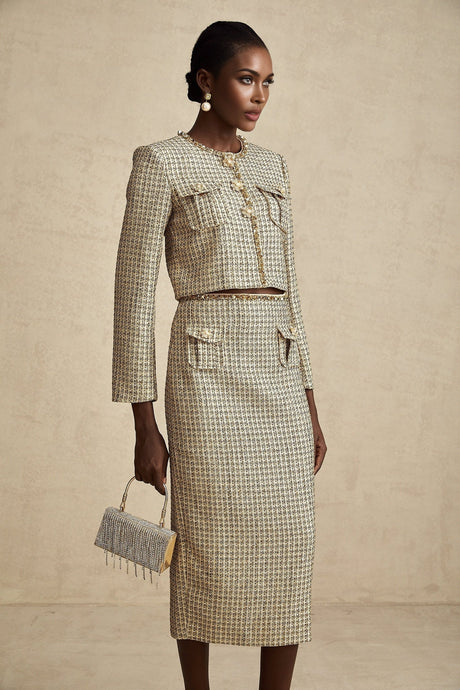 Woman wearing gold tweed sequin jacket and matching skirt set by Aelle standing against plain background