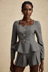 Woman wearing grey herringbone patterned matching set with short sleeve top and shorts standing against plain background
