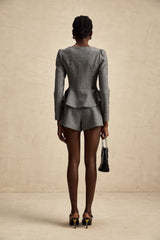 Woman wearing grey herringbone patterned top and matching shorts set standing against plain background