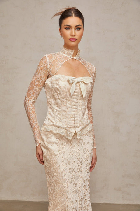 Woman wearing ivory colored matching set with patterned jacquard top and skirt standing against plain background