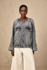 Woman wearing light blue collarless denim jacket with button front closure and chest pockets