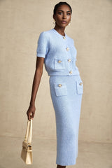Woman wearing light blue knitted sweater and matching midi skirt set standing against plain background