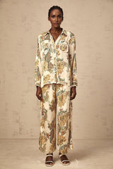 Woman wearing light colored floral print matching shirt and trousers set standing against neutral background