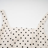 Woman wearing light colored polka dot mini dress with puffed sleeves and gathered skirt