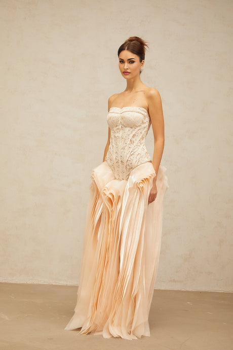 Woman wearing long beige lace corset maxi dress with layered skirt and neutral tones standing in front of plain background