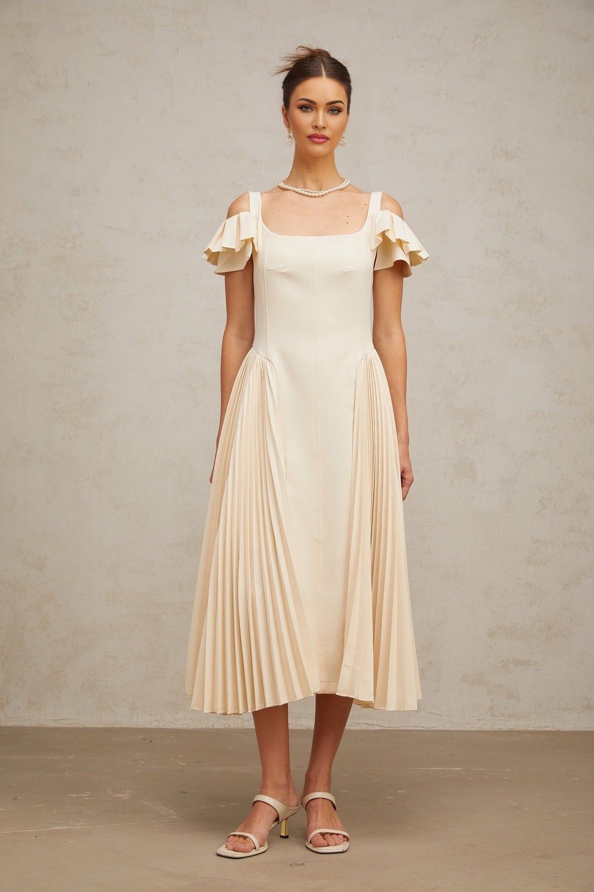 Woman wearing long beige pleated midi dress with flared skirt and neutral tones standing in relaxed pose