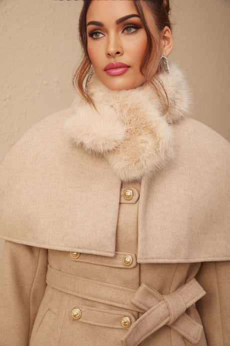 Woman wearing long black faux fur coat with detachable cape collar standing against plain background