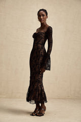 Woman wearing long black flared lace maxi dress with Marlene style silhouette standing against plain background
