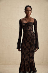 Woman wearing long black lace maxi dress with flared skirt and fitted bodice standing in elegant pose