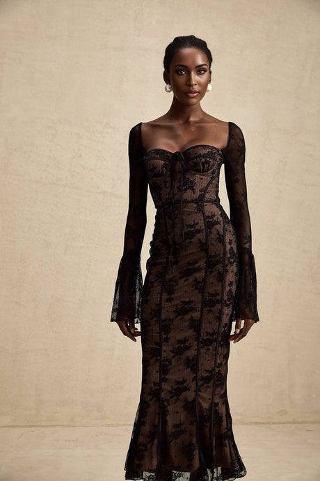 Woman wearing long black lace maxi dress with flared skirt and fitted bodice standing in elegant pose