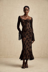 Woman wearing long black lace maxi dress with flared skirt standing in front of plain background