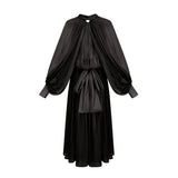 Woman wearing long black pleated satin maxi dress with flowing skirt and fitted bodice