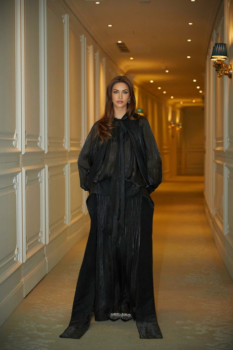 Woman wearing long black pleated satin maxi dress with flowing skirt