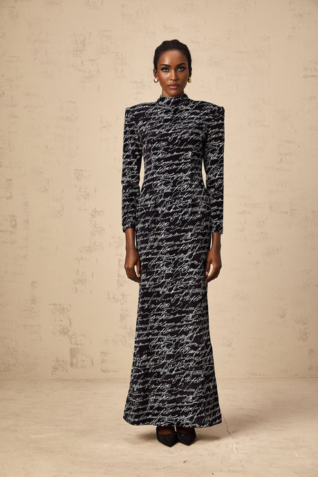 Woman wearing long black velvet maxi dress with jade green lettering printed across the fabric
