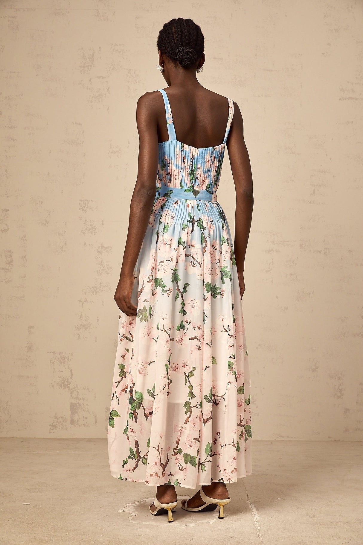 Woman wearing long blue dress with floral print and pleated skirt