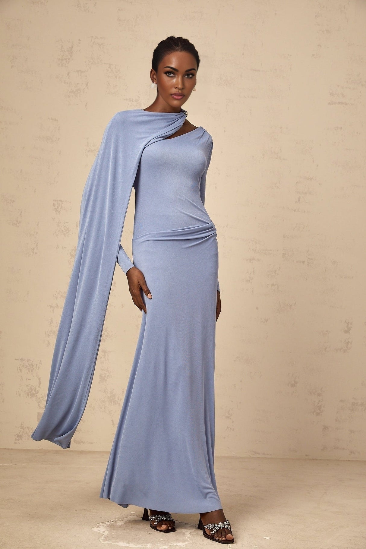 Woman wearing long blue fitted maxi dress with diagonal shawl neckline