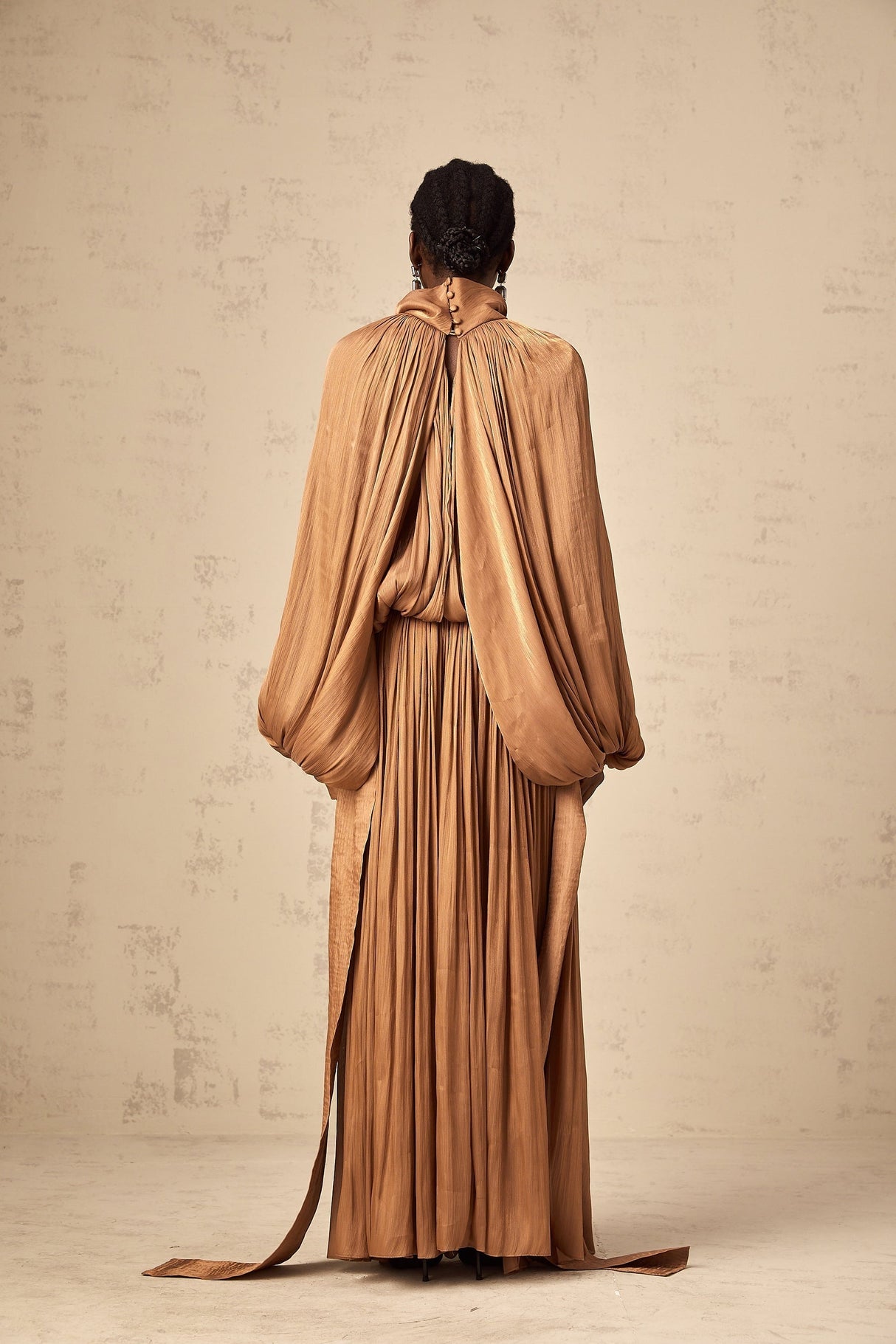 Woman wearing long brown pleated satin maxi dress with flowing skirt and fitted bodice