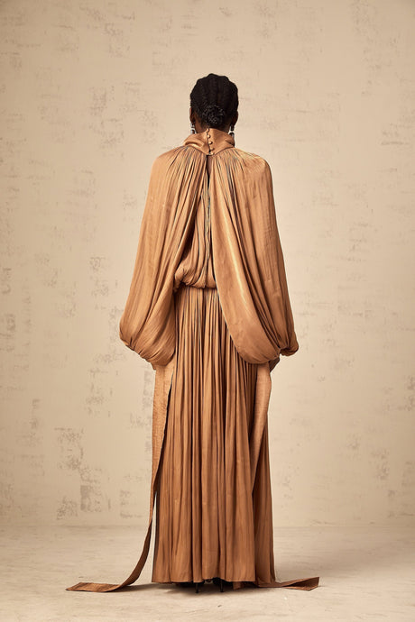 Woman wearing long brown pleated satin maxi dress with flowing skirt and fitted bodice
