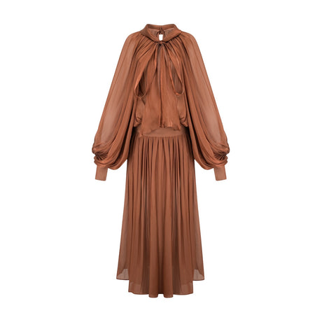 Woman wearing long brown pleated satin maxi dress with flowing skirt and fitted bodice