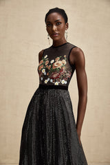 Woman wearing long floral embroidered maxi dress with embellishments against plain background