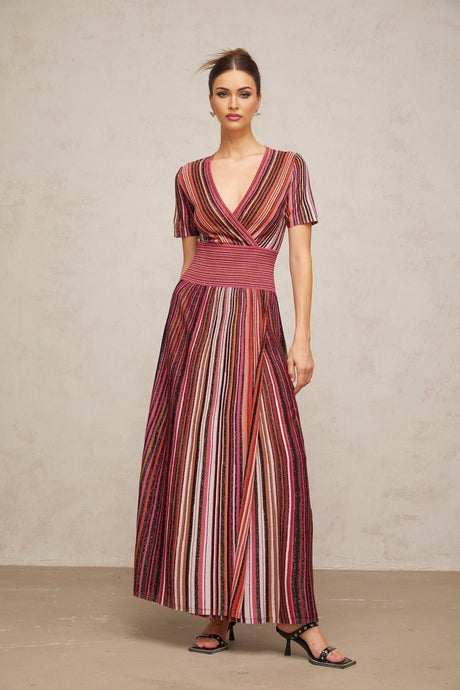 Woman wearing long flowing metallic knit maxi dress with multicolor stripes in shimmering tones standing against plain background