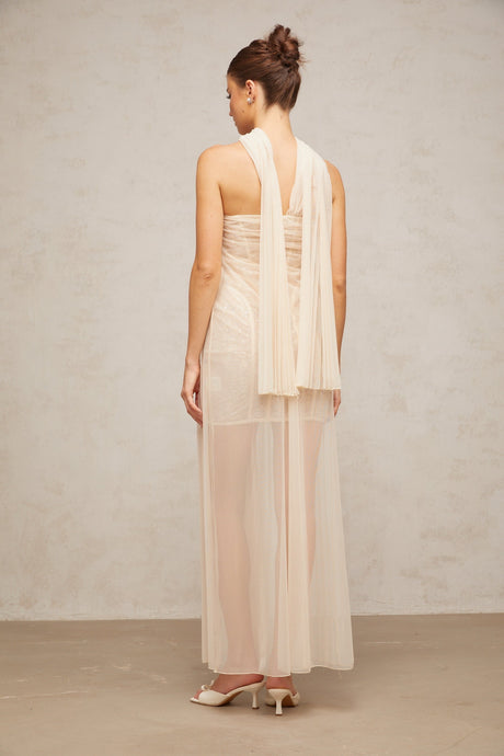 Woman wearing long flowing neutral colored tulle maxi dress with pleated skirt and ribbon detailing on bodice