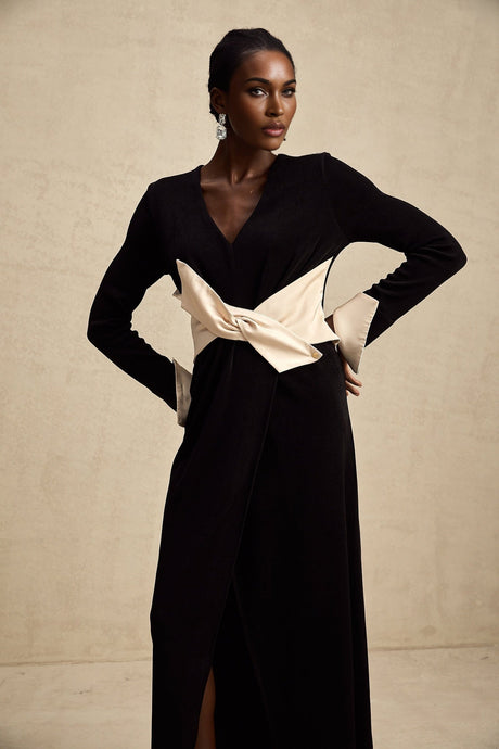 Woman wearing long flowy maxi dress with contrasting colors and v neckline featuring large decorative bow detail