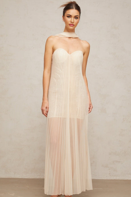 Woman wearing long flowy neutral colored maxi dress with pleated tulle skirt and ribbon detailing on bodice