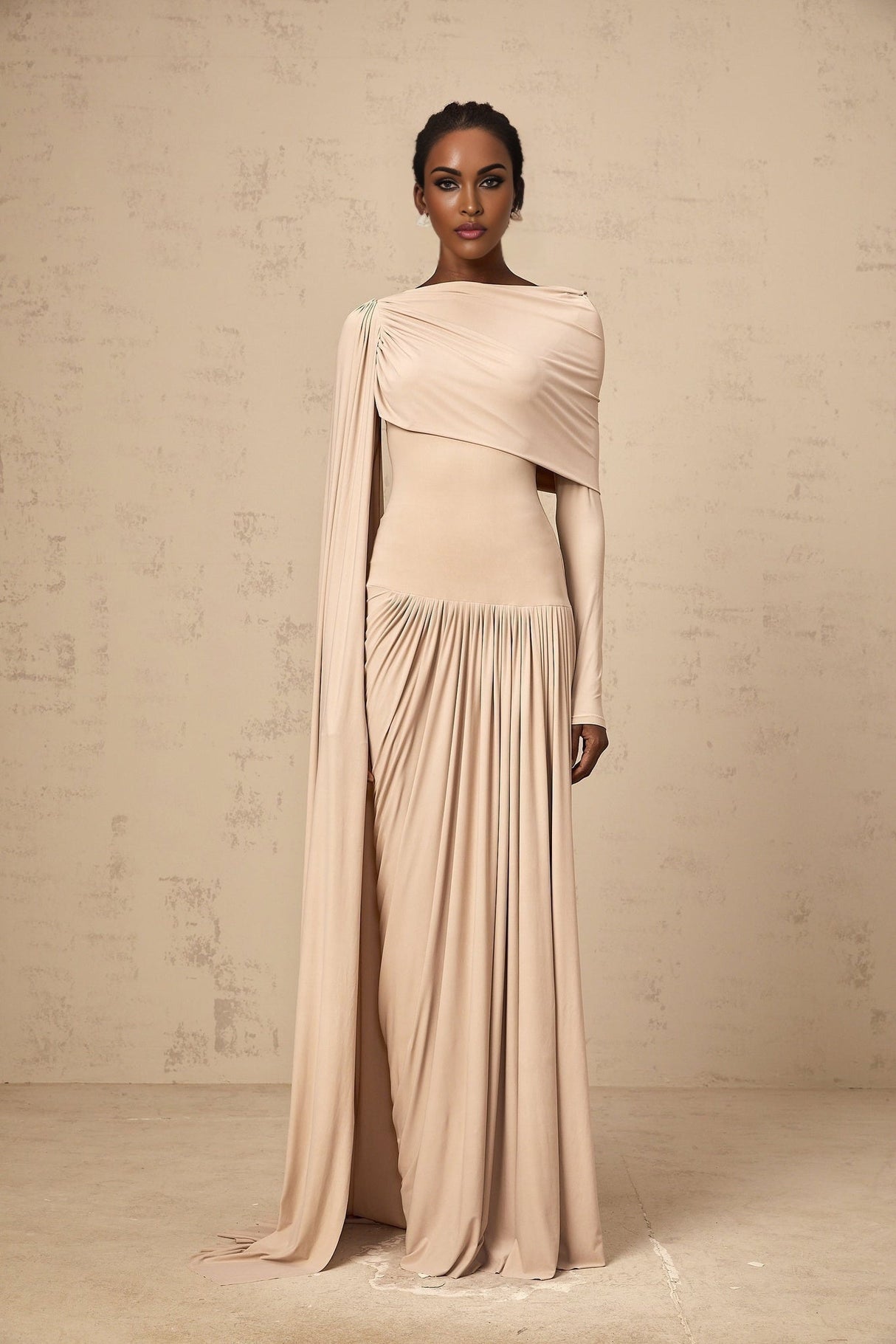 Woman wearing long flowy neutral colored maxi dress with ribbon design details and draped fabric