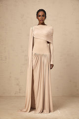 Woman wearing long flowy neutral colored maxi dress with ribbon design details and draped fabric