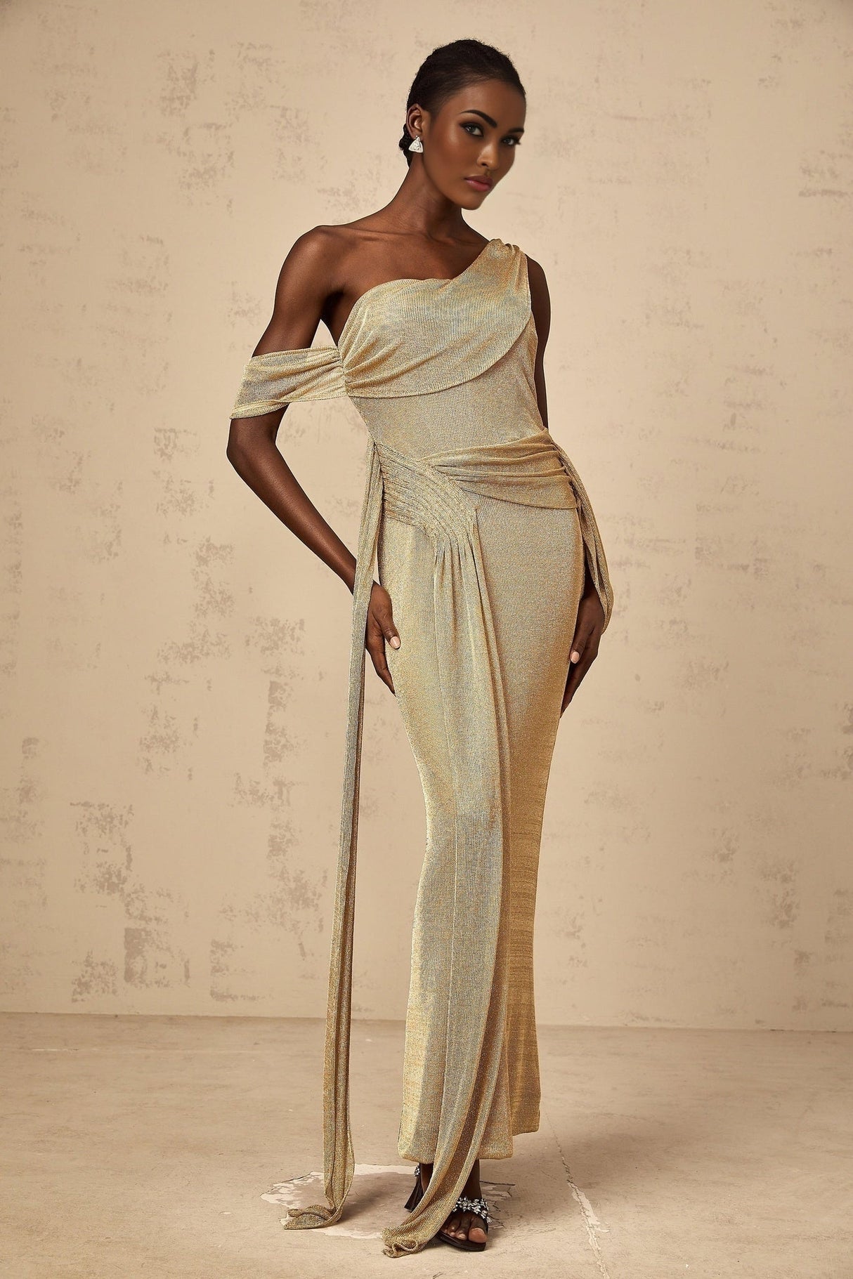 Woman wearing long gold maxi dress with gathered waist and ribbon design detail