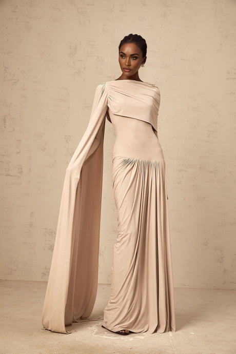 Woman wearing long neutral colored maxi dress with ribbon design and draped details