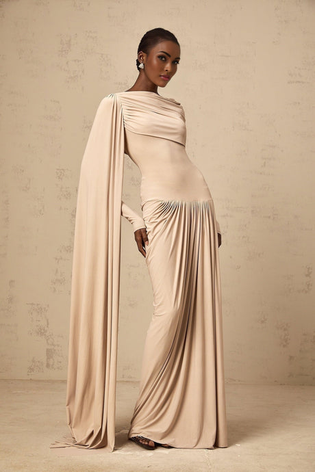 Woman wearing long neutral colored maxi dress with ribbon design details and draped fabric