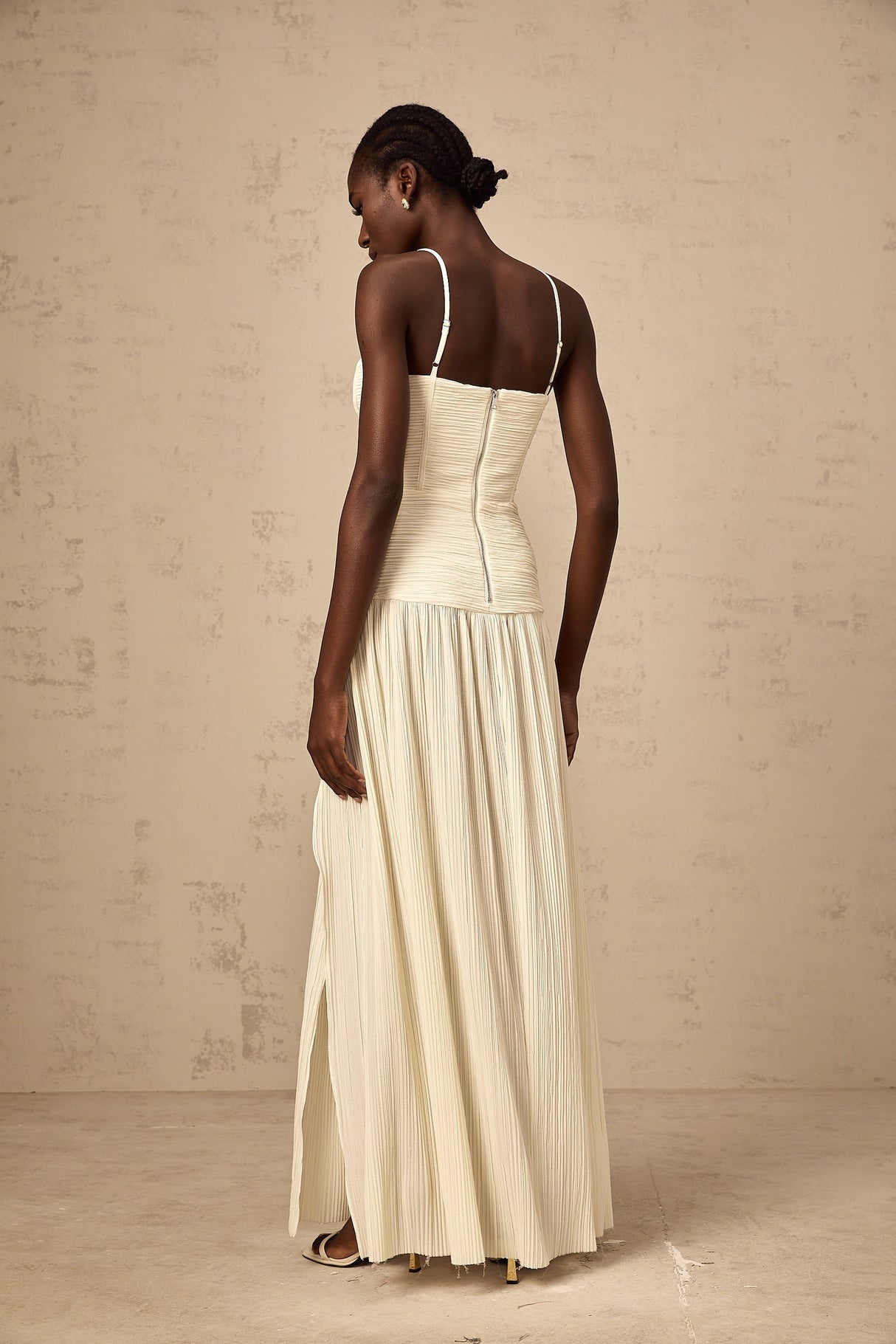 Woman wearing long neutral colored pleated maxi dress with side slit standing in relaxed pose
