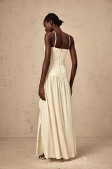 Woman wearing long neutral colored pleated maxi dress with side slit standing in relaxed pose