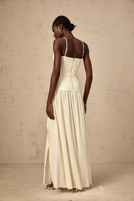 Woman wearing long neutral colored pleated maxi dress with side slit standing in relaxed pose