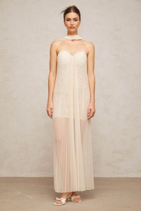 Woman wearing long neutral colored tulle maxi dress with ribbon design and pleated details