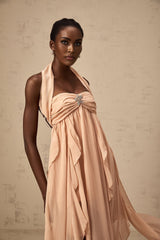 Woman wearing long pink chiffon maxi dress with ruffled halter neck and flowing skirt