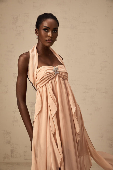 Woman wearing long pink chiffon maxi dress with ruffled halter neck and flowing skirt