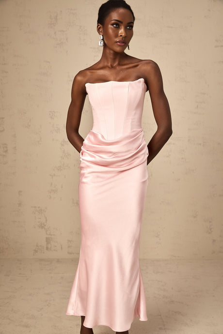 Woman wearing long pink offshoulder maxi dress with flowing skirt standing outdoors