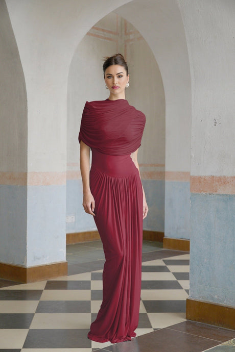 Woman wearing long red asymmetric pleated maxi dress with flowing skirt and one shoulder design