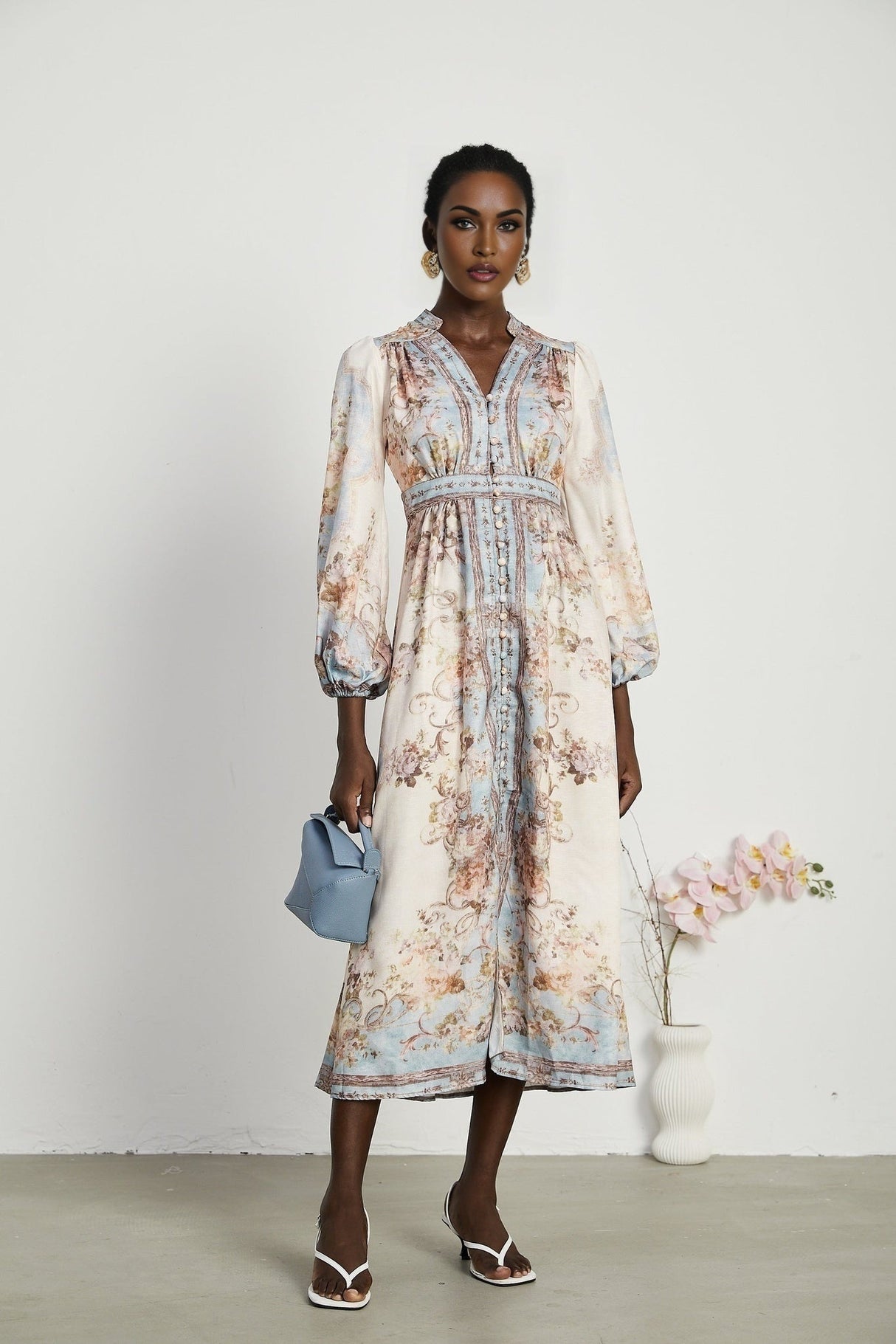 Woman wearing long sleeve floral print boho dress with flowing skirt and v neckline in pastel colors against plain background