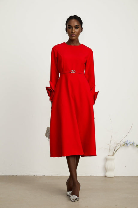 Woman wearing long sleeve red dress with floral pattern standing in front of plain background