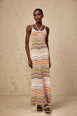 Woman wearing long striped knit maxi dress with multicolored horizontal stripes in pastel shades standing against neutral background