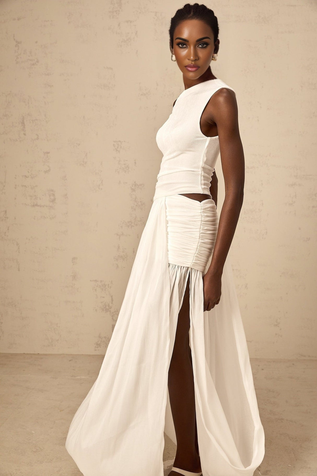 Woman wearing long white dress with one shoulder strap and gathered fabric details flowing to floor length
