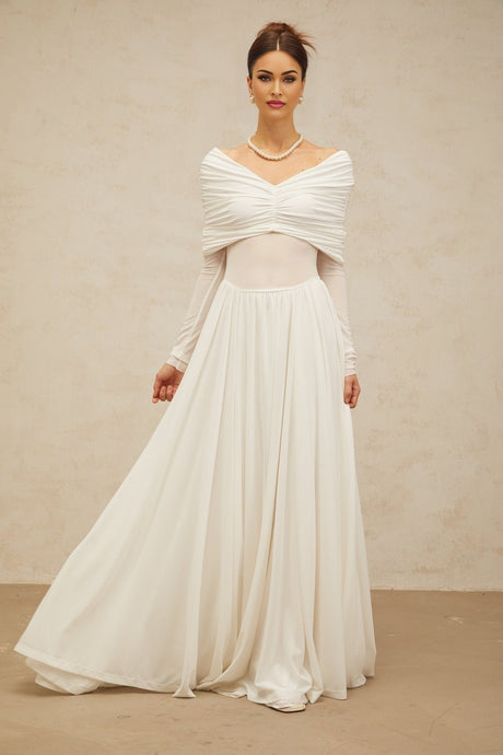Woman wearing long white flowing maxi dress with draped and ruched details standing in elegant pose