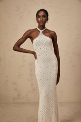 Woman wearing long white halterneck maxi dress with embellished details standing against plain background