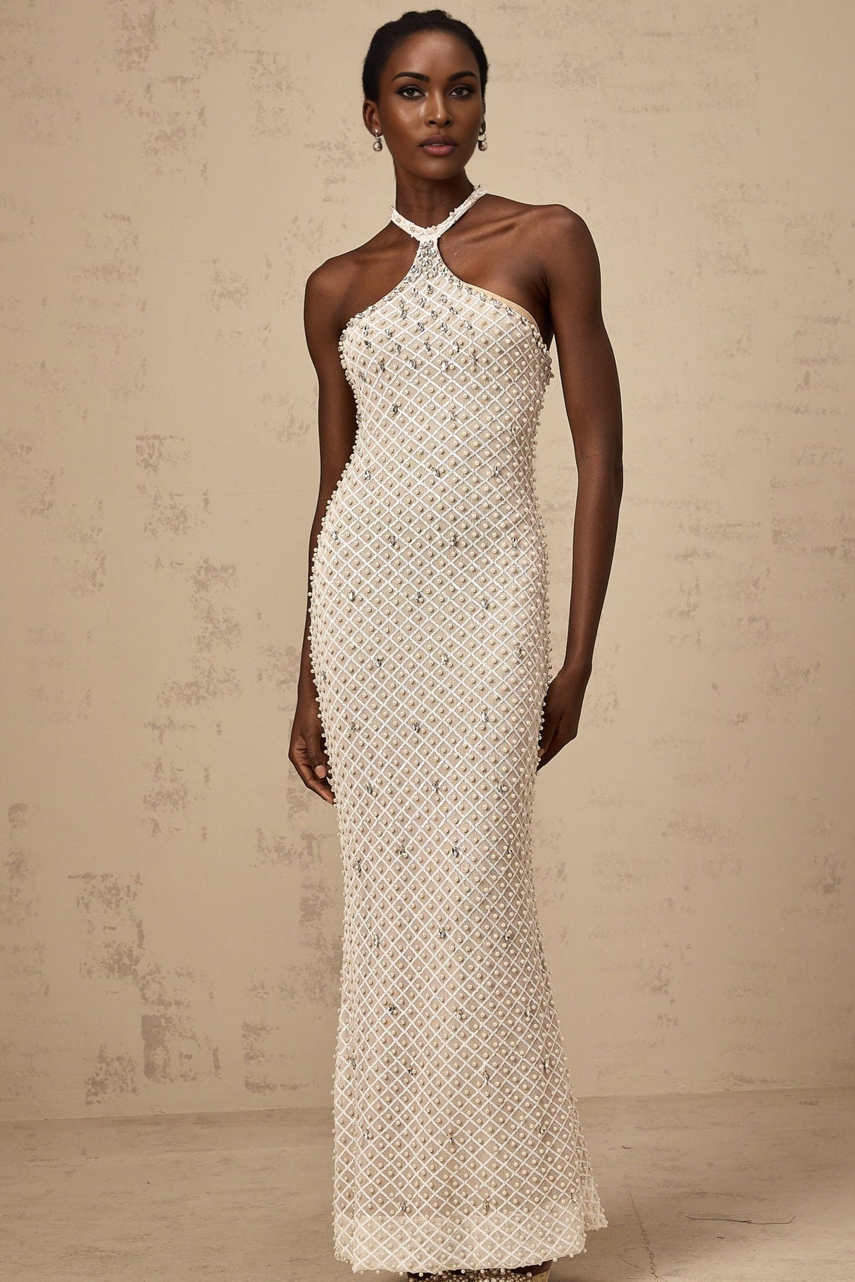 Woman wearing long white halterneck maxi dress with embellished details standing against plain background